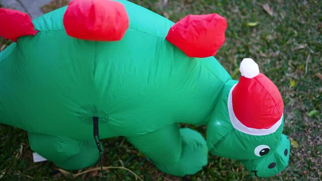 christmas inflatable dinosaur with red hat, christmas garden decoration on green grass, green dinosaur for children