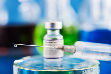 syringe with a drop of Covid-19 vaccine on a needle on a blue background.