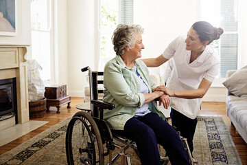 Helping others is a calling. Shot of a smiling caregiver helping a senior woman in a wheelchair at home.