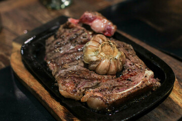 Grilled beef steak meat with rosemary and grilled garlic on grill iron pan.  Close-up. Rustic