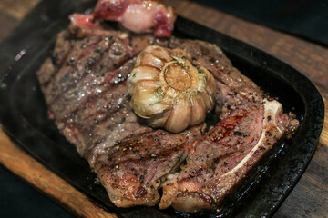 Grilled beef steak meat with rosemary and grilled garlic on grill iron pan.  Close-up. Rustic