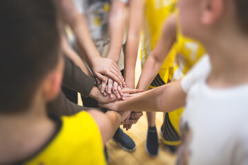 Team of kids children basketball players stacking hands in the court, sports team together holding hands getting ready for the game, playing indoor basketball, team talk with coach, close up of hands