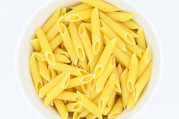 Raw penne rigate pasta, in a white bowl, isolated on a white background
