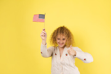 A young happy girl with a smile on her face holds an American flag in her hands. Symbol of patriotism and freedom.