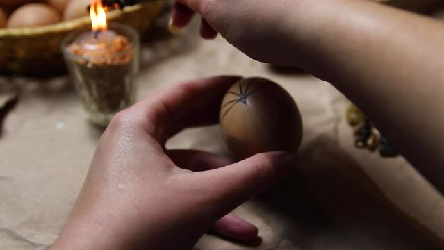 Female hand holding pen, pysachok, and egg and painting it. Preparing for painting Ukrainian Easter eggs decorated with folk designs using a wax resist method. Pysanka, Easter egg. Fragile