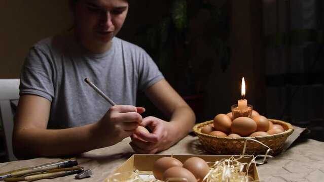 Young woman holding egg near flame and painting it by pencil. Preparing for painting Ukrainian Easter eggs decorated with folk designs using a wax resist method. Pysanka, Easter egg. Night. Handmade