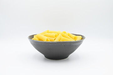 Raw Tortiglioni pasta, in a dark grey bowl, isolated on a white background