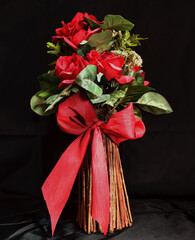 Red Rose artificial flowers in a wicker vase on a black background with a large red bow 