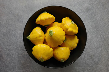 A black bowl with raw yellow sunburst squash vegetables seen from directly above