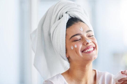 Not a wrinkle in sight. Shot of a beautiful young woman applying moisturizer to her skin in the bathroom at home.
