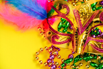 Carnival mask and beads on yellow background. Mardi Gras concept. Fat Tuesday symbol.