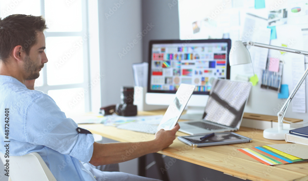 Poster portrait of young designer sitting at graphic studio in front of laptop and computer while working o