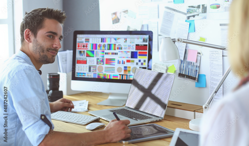 Poster portrait of young designer sitting at graphic studio in front of laptop and computer while working o