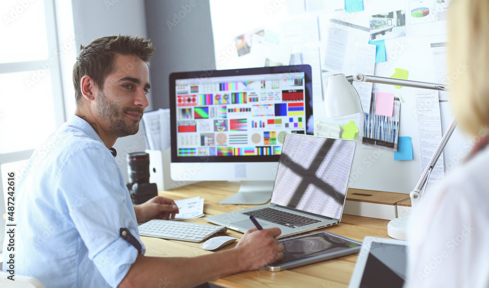 Poster portrait of young designer sitting at graphic studio in front of laptop and computer while working o
