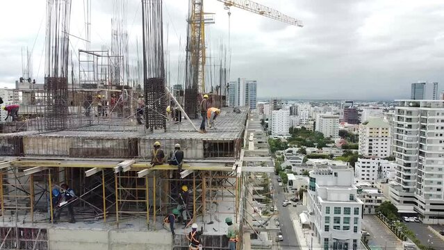 Vuelo a&eacute;reo con giro 180 grados captando obreros trabajando proyecto inmobiliarios, con fondo de la cuidad urbana de santo domingo 