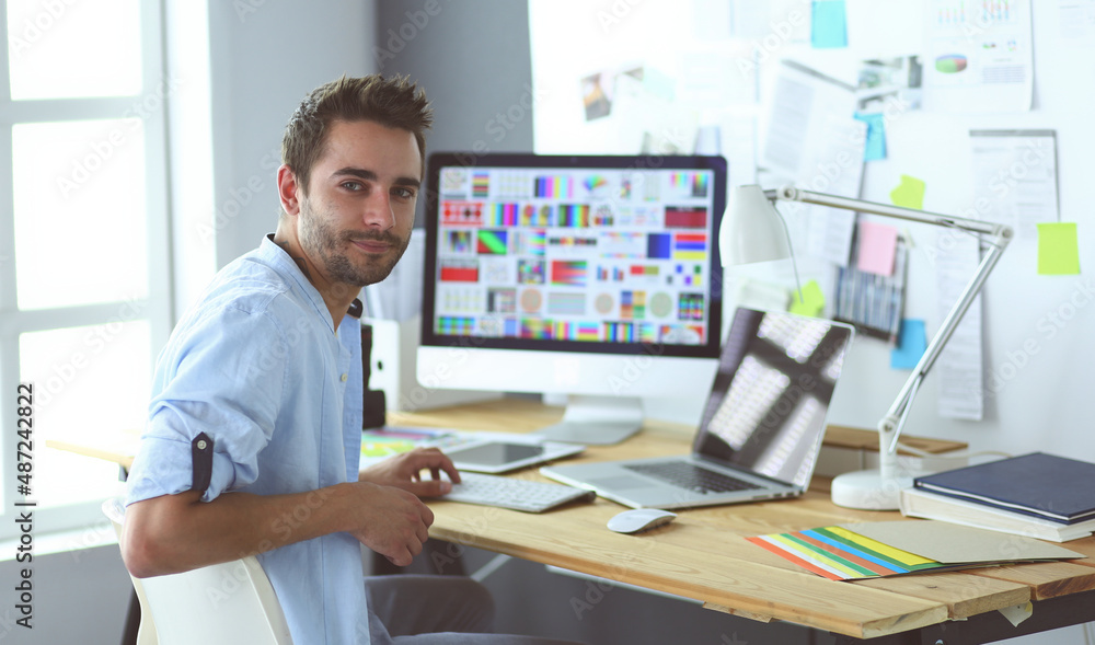 Poster portrait of young designer sitting at graphic studio in front of laptop and computer while working o