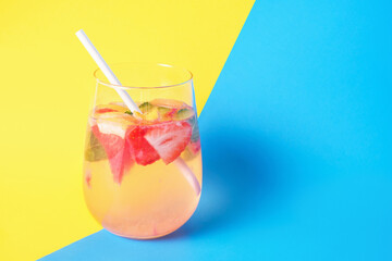 Glass with fruity summer drink and mint on blue and yellow background close-up.