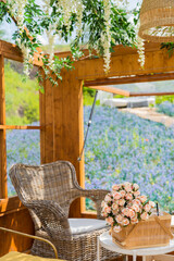 Cozy wooden cottage with picnic basket with flowers bouquet with rattan table and chairs overlooking blue flower field from the window in the garden