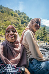 Two Indonesian girl smiling pose when she got on the top of mountain and down river valley. the photo perfect for family holidays background, nature pamphlet and advertising brochure.