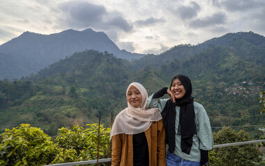 Fototapeta na wymiar Two Indonesian girl smiling pose when she got on the top of mountain. the photo perfect for family holidays background, nature pamphlet and advertising brochure.
