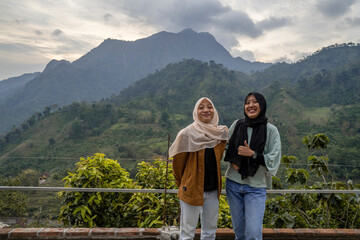 Fototapeta na wymiar Two Indonesian girl smiling pose when she got on the top of mountain. the photo perfect for family holidays background, nature pamphlet and advertising brochure.