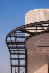 Curved metal awning structure with corrugated steel roof of modern building in construction site against blue sky in vertical frame