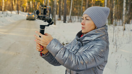 The Woman Professional Videographer Holding Smartphone on 3-axis Gimbal Stabilization Device in Winter. Pro Equipment Helps to Make High Quality Video on Phone. Cinematographer Operator. Slow Motion