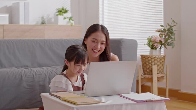 Asian young mother and her daughter have video call conference with family having fun together.Happiness Mom and little girl looking at mobile phone and waving hand with video chat to grandmother