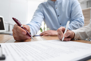 Businesspeople signing contract at table in office, closeup