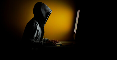Hooded hackers stealing information from a computer on a yellow background in a dark room