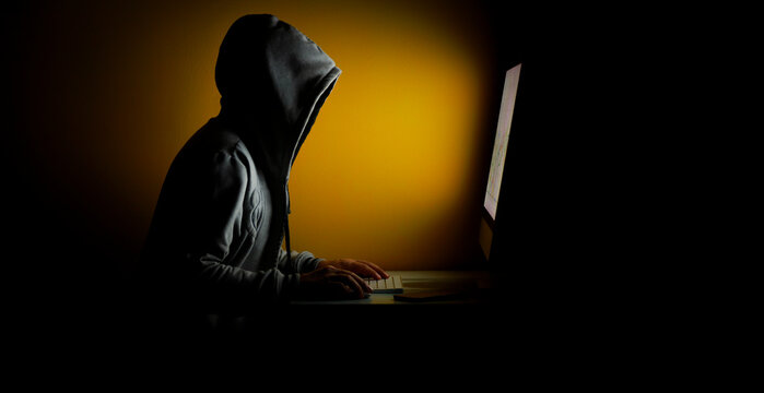 Hooded hackers stealing information from a computer on a yellow background in a dark room