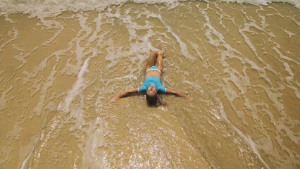 Crazy madwoman daring funny woman lying on shallow water sea. Top view happy slightly tipsy woman enjoying her vacation on a tropical island. Smiling girl funny posing. Concept summer holidays