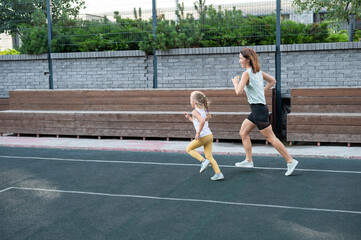Obraz premium Caucasian woman goes in for sports with her daughter outdoors. A schoolgirl and her mother are running around in the stadium.