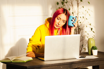 an adult girl with pink hair at a laptop