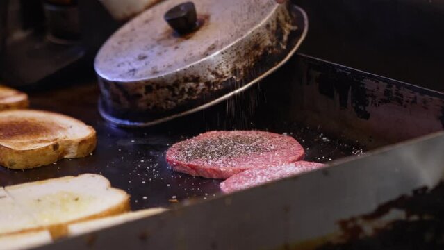 Chef seasons hamburger patties sizzling on flat top grill, slow motion 4k