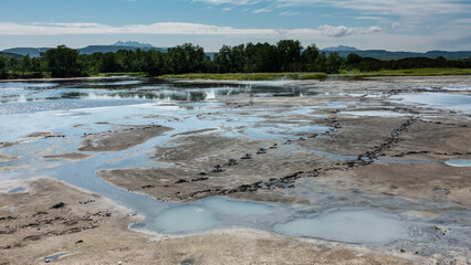 In the caldera of an extinct volcano there are small lakes with thermal water. Sulphurous deposits on the soil. Bear tracks are visible. Mountain range and green vegetation against the sky. Kamchatka.