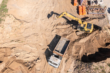 heavy equipment excavator and dump truck on construction site. aerial view from flying drone.