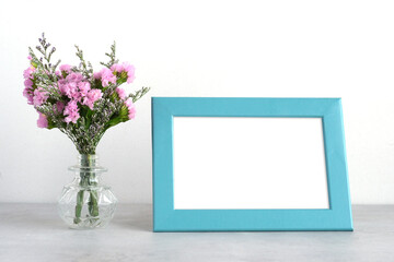 Flower bouquet in glass vase and blank blue wooden frame on table background with copy space , Banner for mock up, template