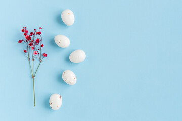 Easter minimal composition with eggs and flowers on the blue background. Easter concept. Copy space, flat lay.