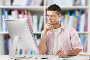 Young male student watching education webinar using laptop writing notes doing research on the internet