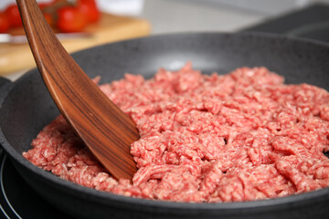 Frying pan with raw minced meat on induction stove, closeup