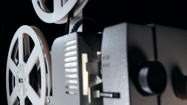 8mm movie projector playing in dark at theater. White reels with tape film rotating. Analog player. Retro old-fashioned. Vintage objects, entertainment, nostalgia, festival equipment concept