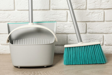 Plastic broom with dustpan near white brick wall indoors
