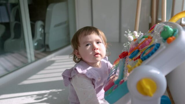 Caucasian baby girl at the balcony in perplexity and looking at camera while playing with a toy table