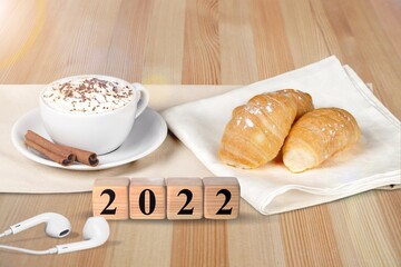 Wooden cubes with number 2022 on a table with coffee, croissant