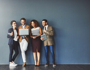The connected team is an efficient team. Studio shot of a group of businesspeople using wireless technology together while standing in line against a gray background.