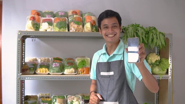 Asian male greengrocer showing vegetables and showing a phone screen