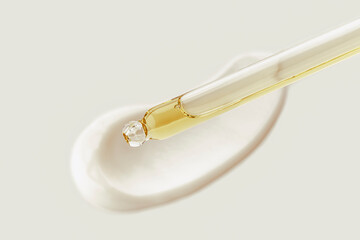 Cosmetic pipette with drops of oil, on the background of white cosmetic cream smear.