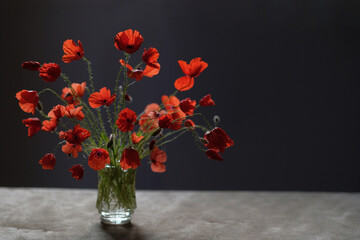 Glass bottle of red poppies stands on a black stone surface.