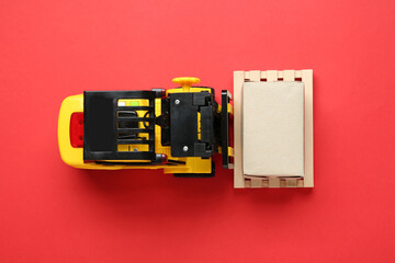 Toy forklift with wooden pallet and box on red background, top view © New Africa